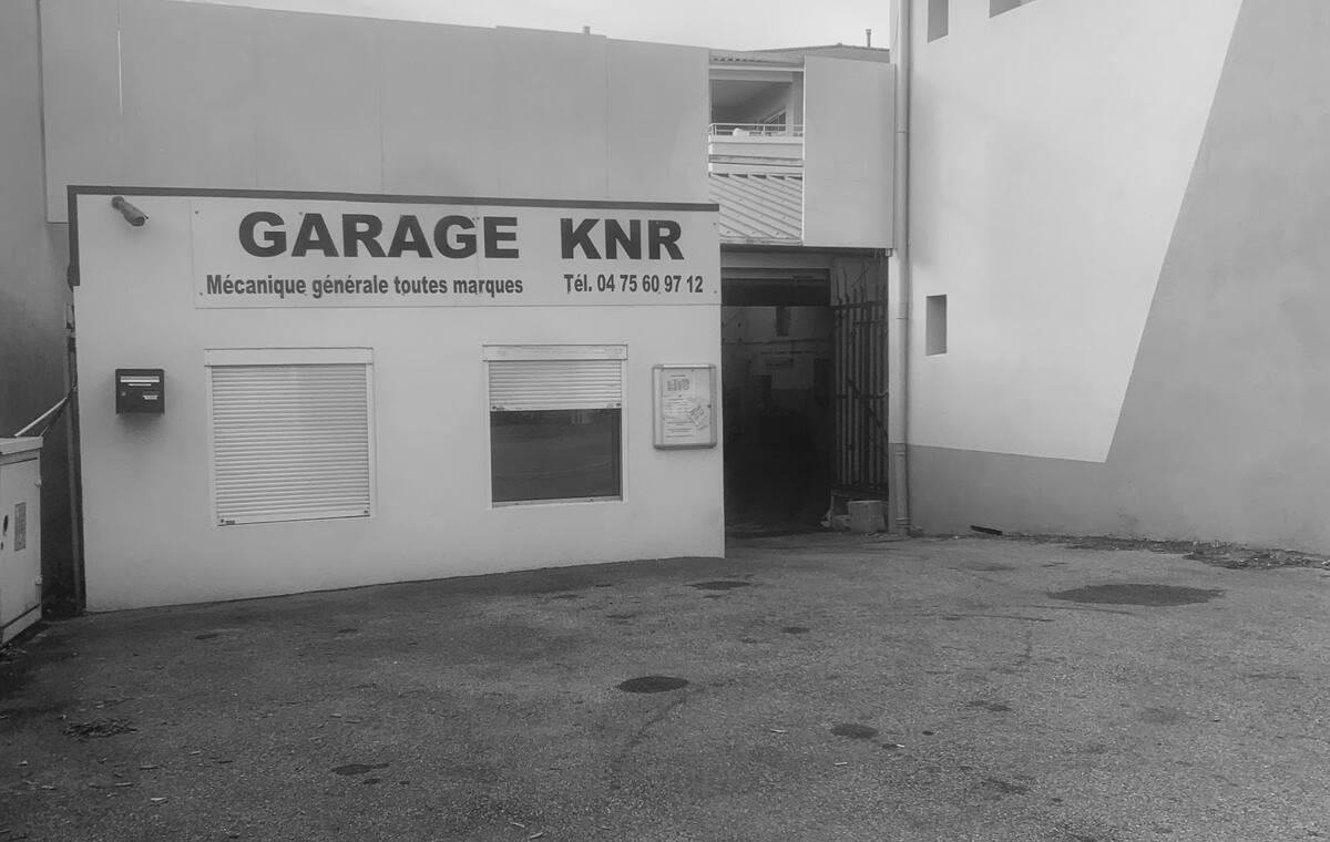 La façade blanche du Garage KNR à Portes-lès-Valence, avec l’enseigne jaune « Garage KNR, mécanique générale toutes marques » et la cour devant